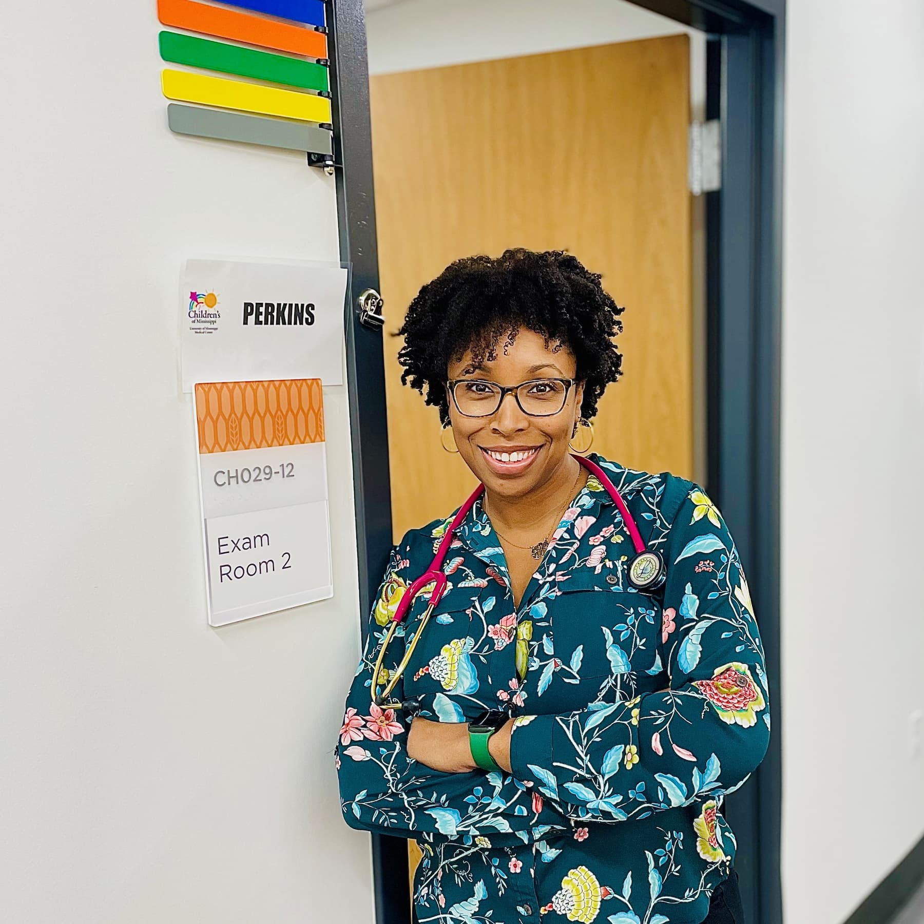 Dr. Jessica Perkins wearing scrubs and a stethoscope while standing in an exam room doorway.